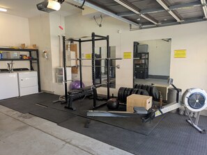 Une salle de sport équipée d’un support à squats, de disques de poids, d’un banc, d’un ballon lesté et d’un ventilateur.