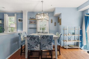 Un coin repas comprenant une table et des chaises, un lustre et une fenêtre avec des stores.