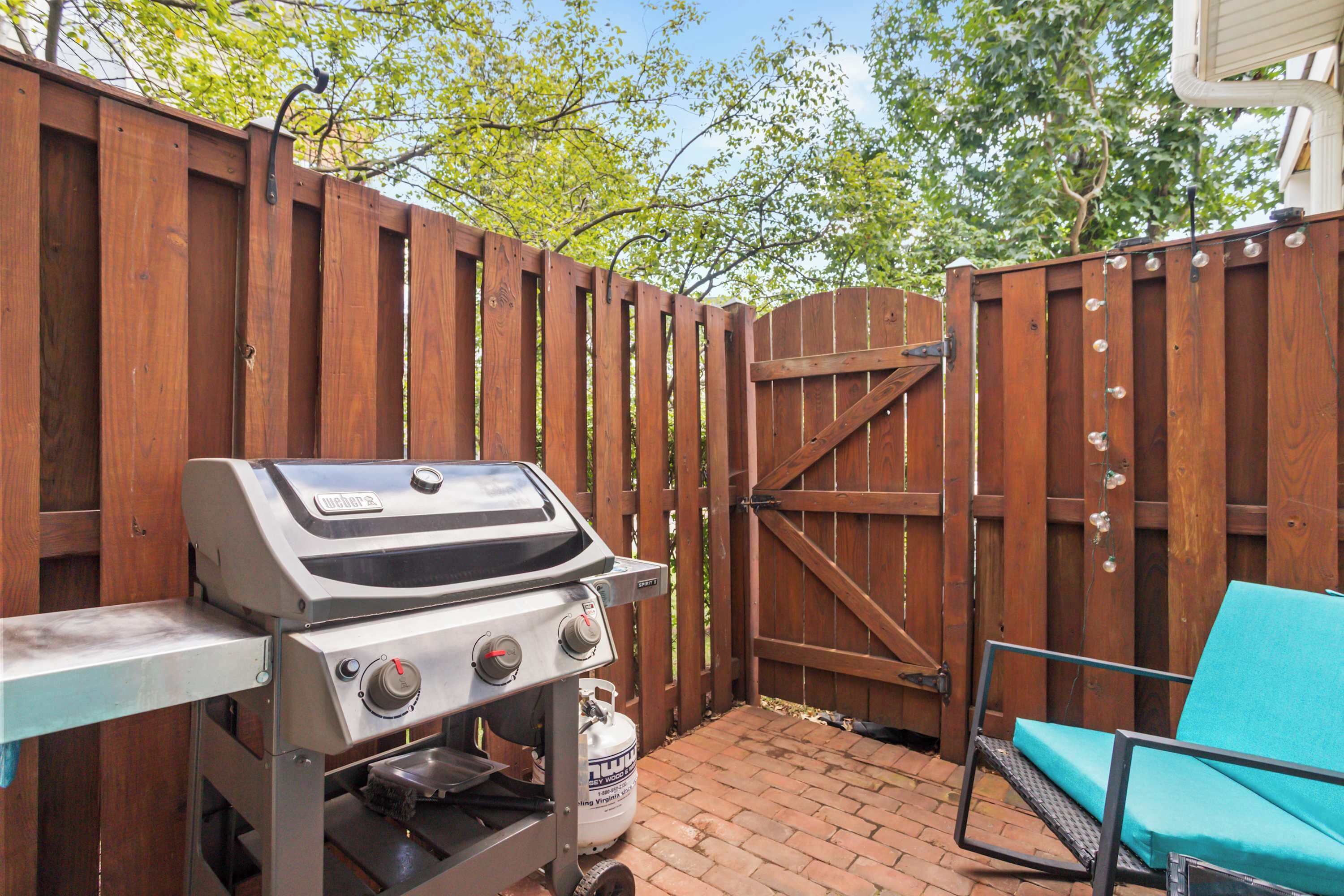 An outdoor patio with a grill, a wooden gate, and a blue chair.