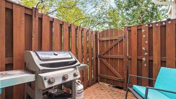 An outdoor patio with a grill, a wooden gate, and a blue chair.