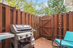 Une terrasse extérieure avec un barbecue, une porte en bois et une chaise bleue.