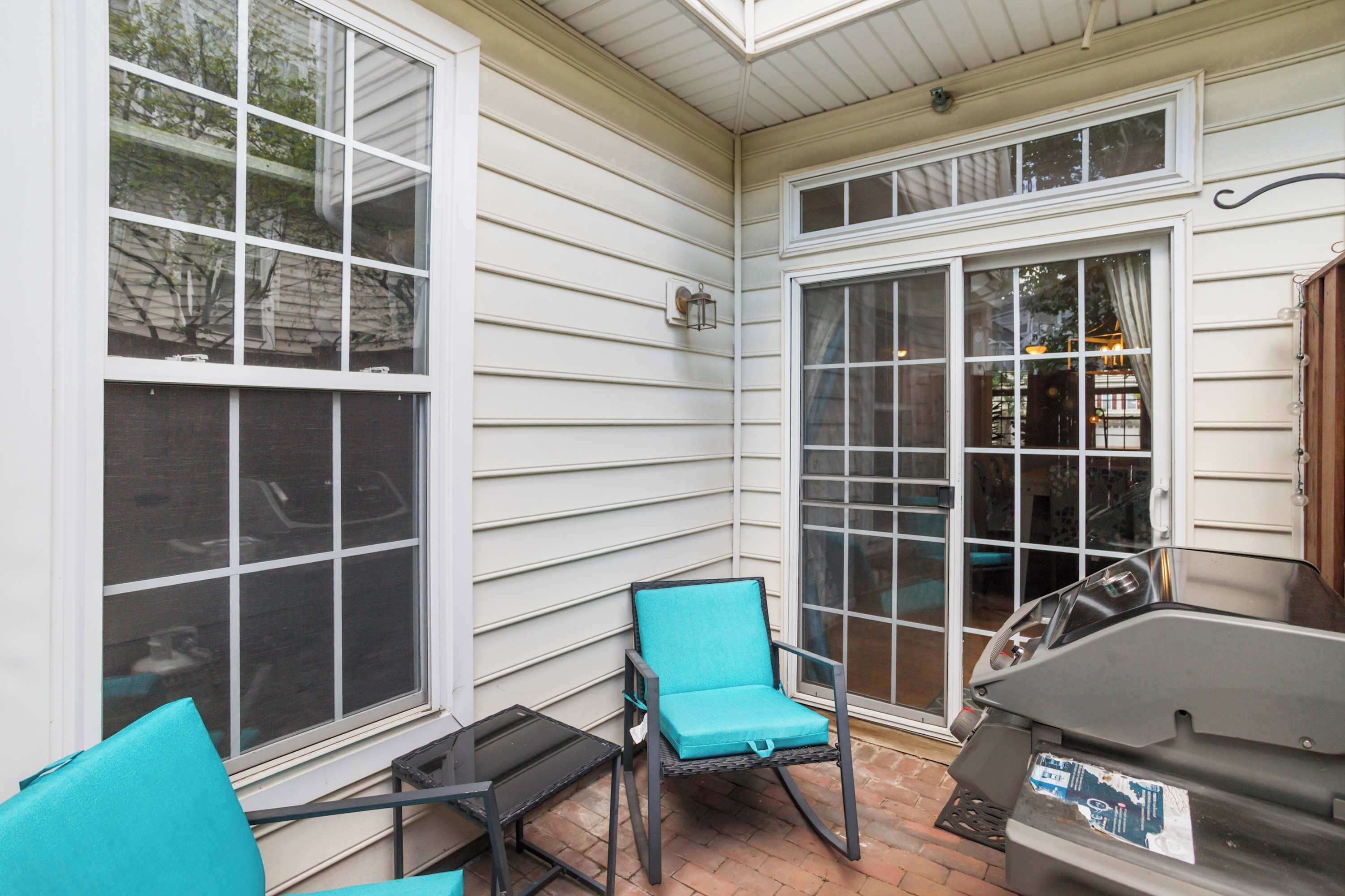 A covered patio area with a grill, a table, and two chairs.