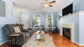 A living room with a fireplace, a ceiling fan, and a television.