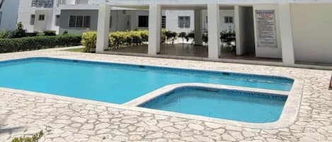 Un immeuble résidentiel à plusieurs étages doté d’une piscine et d’un patio dallé de pierres.