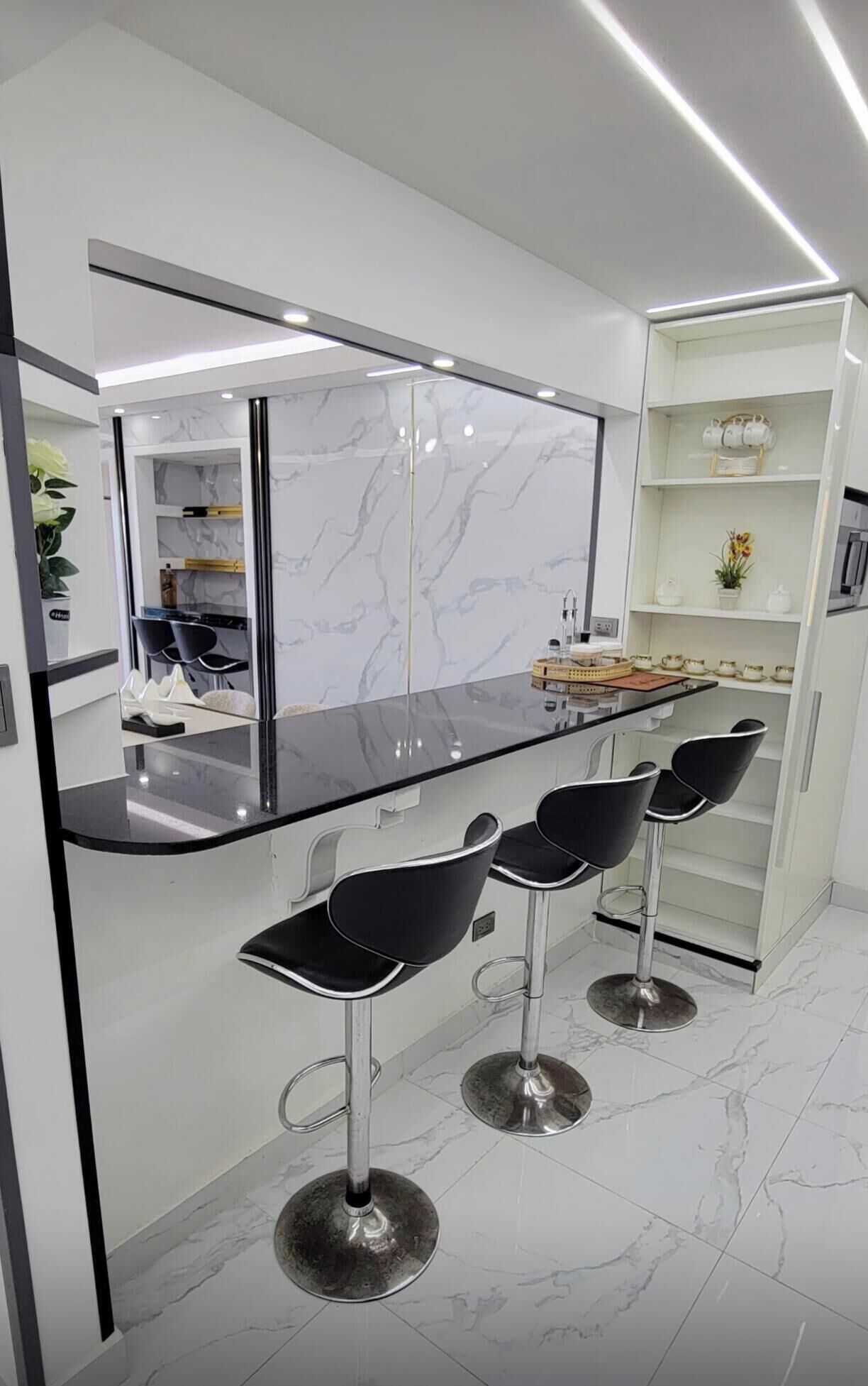A modern kitchen with a marble backsplash, black bar stools, and a built-in island with a black countertop.