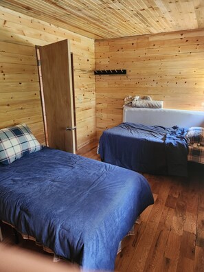 A room with two beds, wooden walls, a door, and a small seating area with a bench. - Hunter's Paradise in Northeast Montana (Culbertson)
