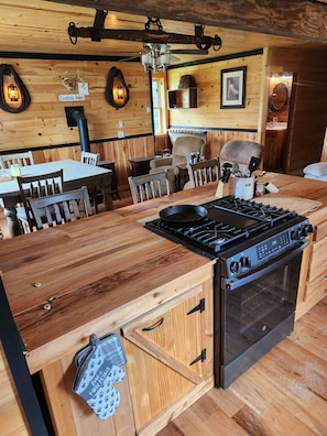 A rustic kitchen with wooden cabinetry, a stove, and a dining area with wooden chairs and a table.