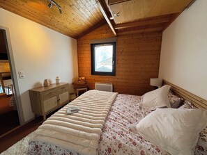 A bedroom with a wooden ceiling, a bed with a floral bedspread, a nightstand, and a window.