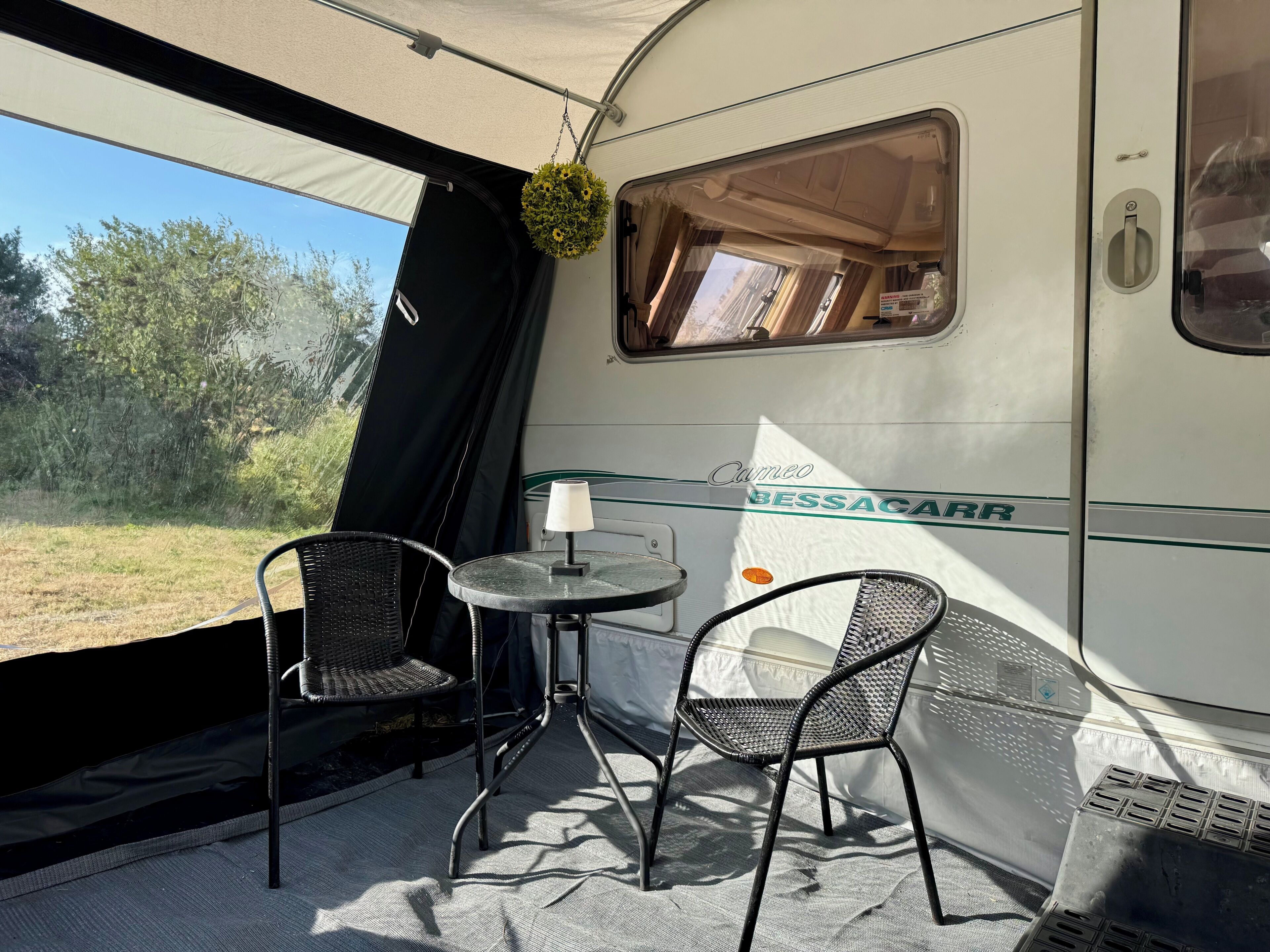 A travel trailer interior with two chairs, a table, and a hanging plant.
