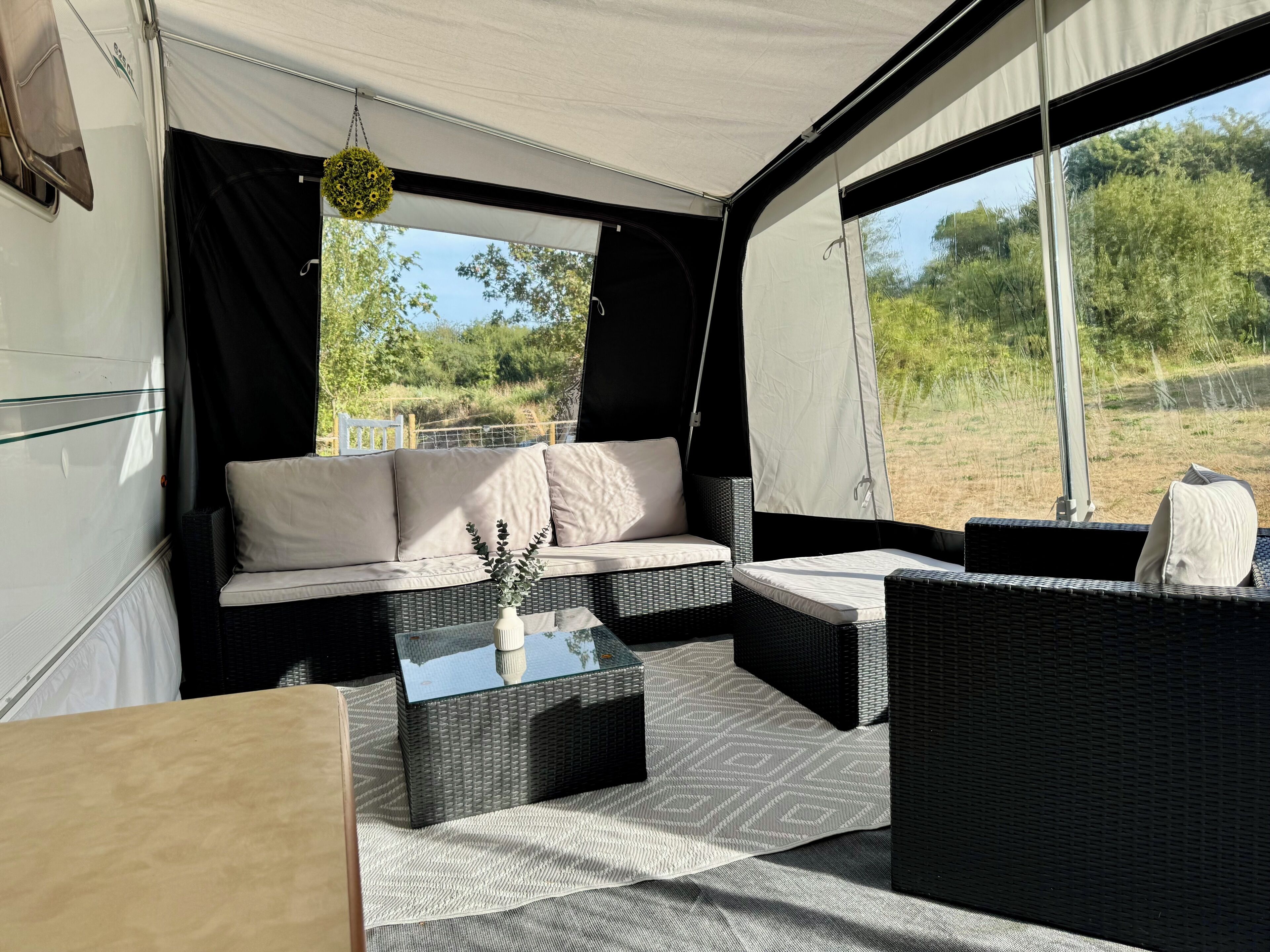 A tented accommodation with a sofa, two chairs, a table, and a hanging plant.