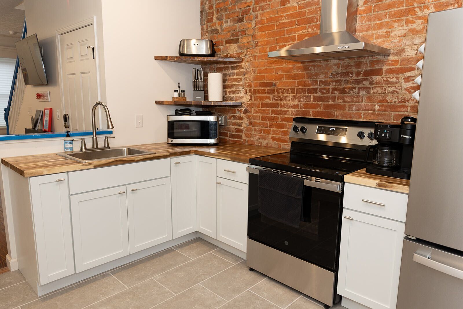Una cocina con gabinetes blancos, estufa de acero inoxidable, microondas y pared de ladrillo.