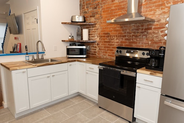 A kitchen with white cabinets, a stainless steel stove, a microwave, and a brick wall.