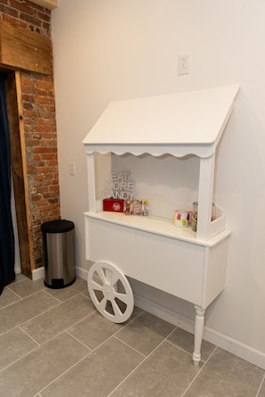 Un carrito de dulces blancos con un letrero que dice 'EAT MORE CANDY' frente a una pared de ladrillo y un piso de baldosas.