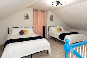 A bedroom with two beds, a ceiling fan, and a staircase with a blue railing.