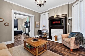 Een woonkamer met een open haard, een bank, een salontafel en een televisie waarop 'NETFLIX' staat.