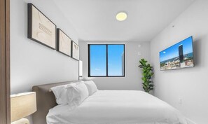 A hotel room with a bed, a window, a plant, and framed pictures on the wall. - 501 First Miami | 2BR w/ Pool near Bayfront Park (Miami)