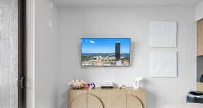 A room with a television mounted on the wall displaying a cityscape, a wooden cabinet with decorative items, and a door with a textured wall. - 501 First Miami | 2BR w/ Pool near Bayfront Park (Miami)
