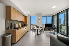 Eine moderne Küche mit Holzschränken, einer Edelstahlspüle und einem eingebauten Backofen. Es gibt eine Essecke mit einem runden Tisch und Stühlen, sowie ein großes Fenster mit Blick auf die Stadt.