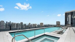 Ein Pool auf dem Dach mit Blick auf die Stadtlandschaft, eine Lounge mit Sitzgelegenheiten und einem klaren Himmel.