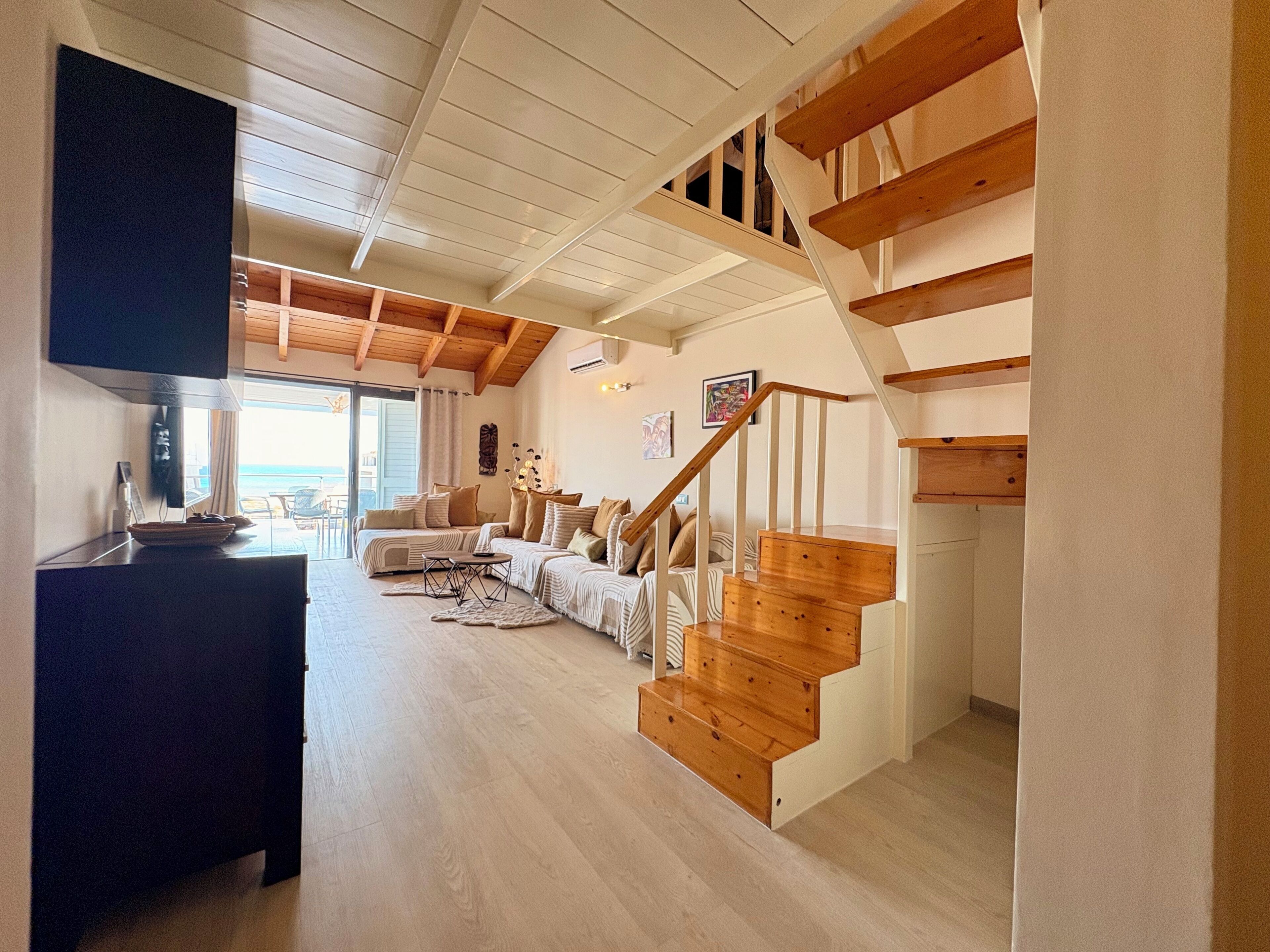 A spacious living area with a wooden staircase, a sofa set, and a television.