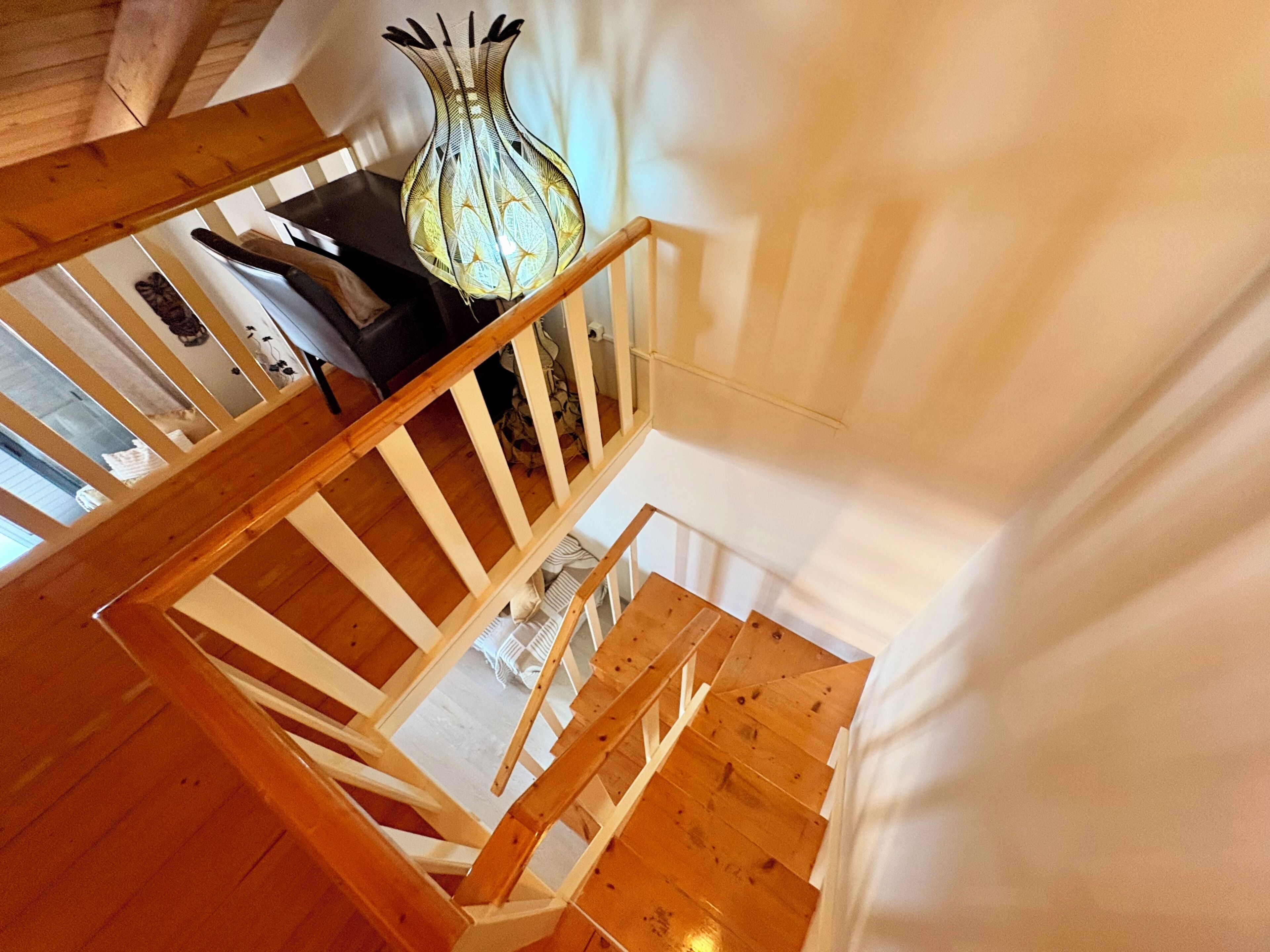 Eine Holztreppe mit weißer Handläufe und einer Vase auf der Podestfläche.
