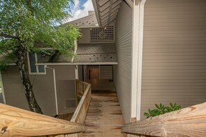 Een houten terras dat leidt naar een huis met een overdekte veranda en een boom.