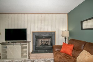 Ein Wohnzimmer mit Kamin, Fernseher und einem braunen Ledersofa.