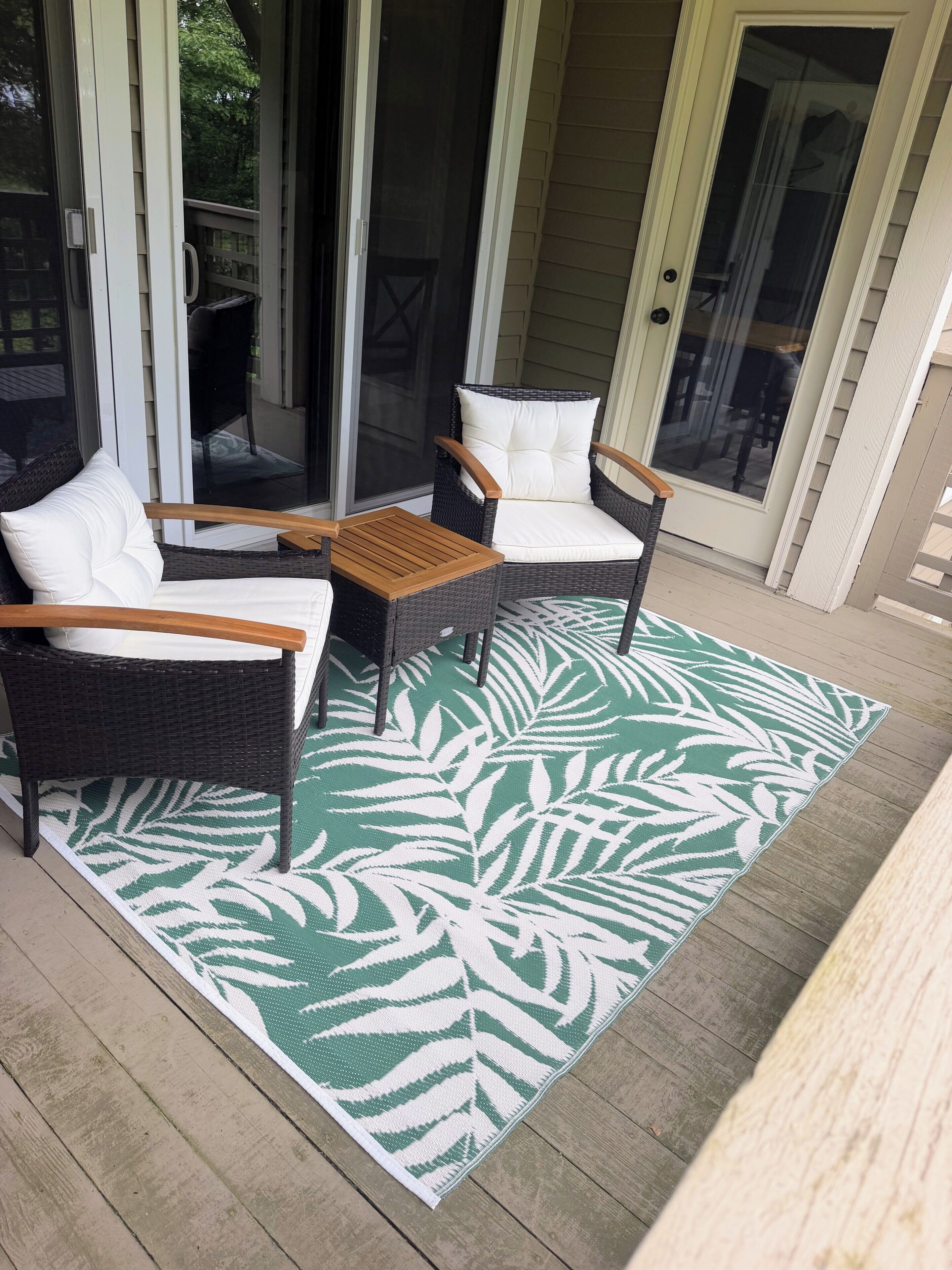 A covered patio area with two wicker chairs and a wooden table, a green and white patterned rug, and a sliding glass door.
