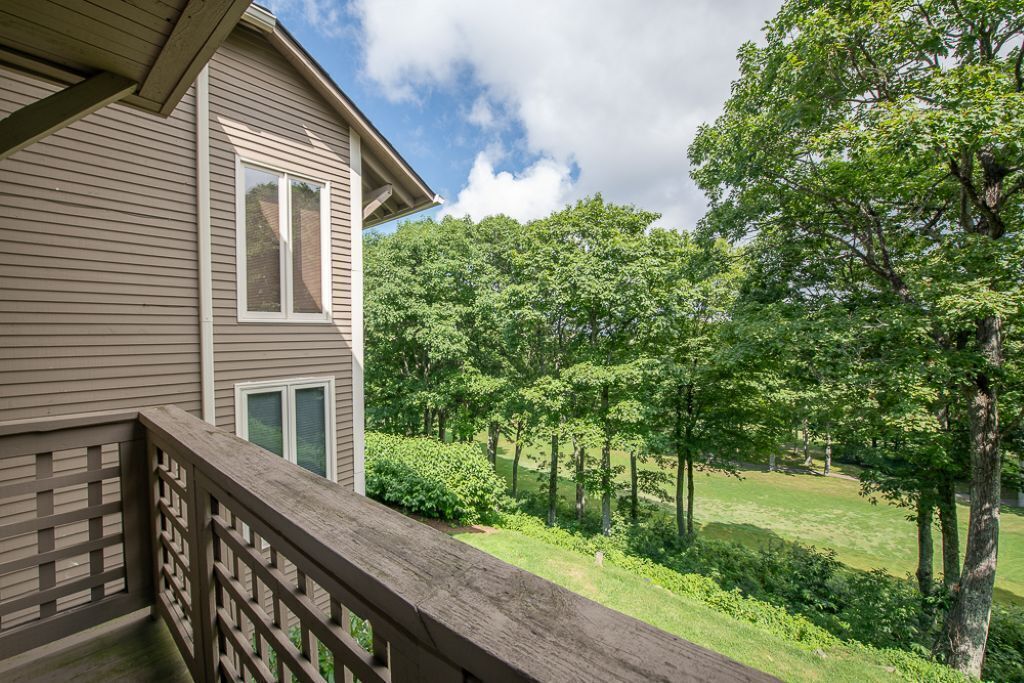 A residential building with a wooden deck and a view of a green landscape with trees.