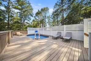 Une terrasse en bois avec une piscine, des chaises longues et un espace délimité par une clôture.