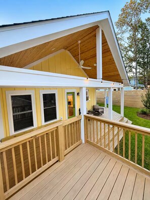 Eine Holzterrasse mit überdachtem Bereich, einem Deckenventilator und einer kleinen Sitzgelegenheit im Freien.