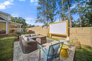 An outdoor patio with a large screen, wicker furniture, and a wooden fence. - Outdoor Movie Theater/ Private POOL & Hot Tub/ Fun (Ocean Isle Beach)