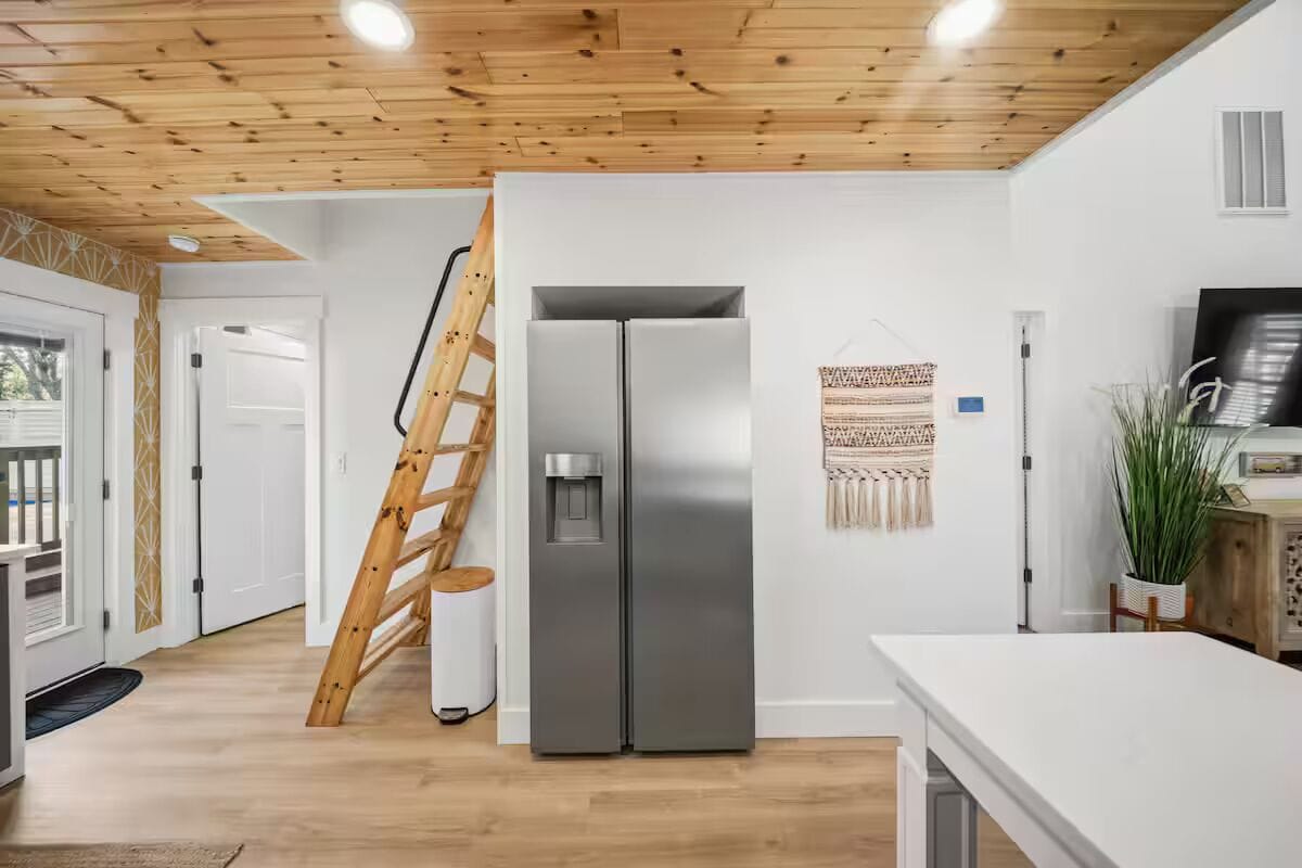 A modern kitchen with a stainless steel refrigerator, wooden ceiling, and a ladder leaning against the wall.
