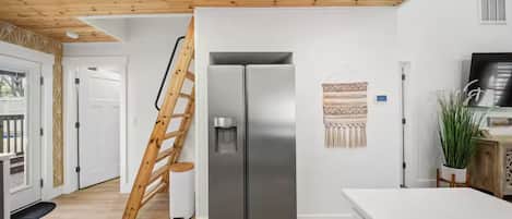 A modern kitchen with a stainless steel refrigerator, wooden ceiling, and a ladder leaning against the wall.