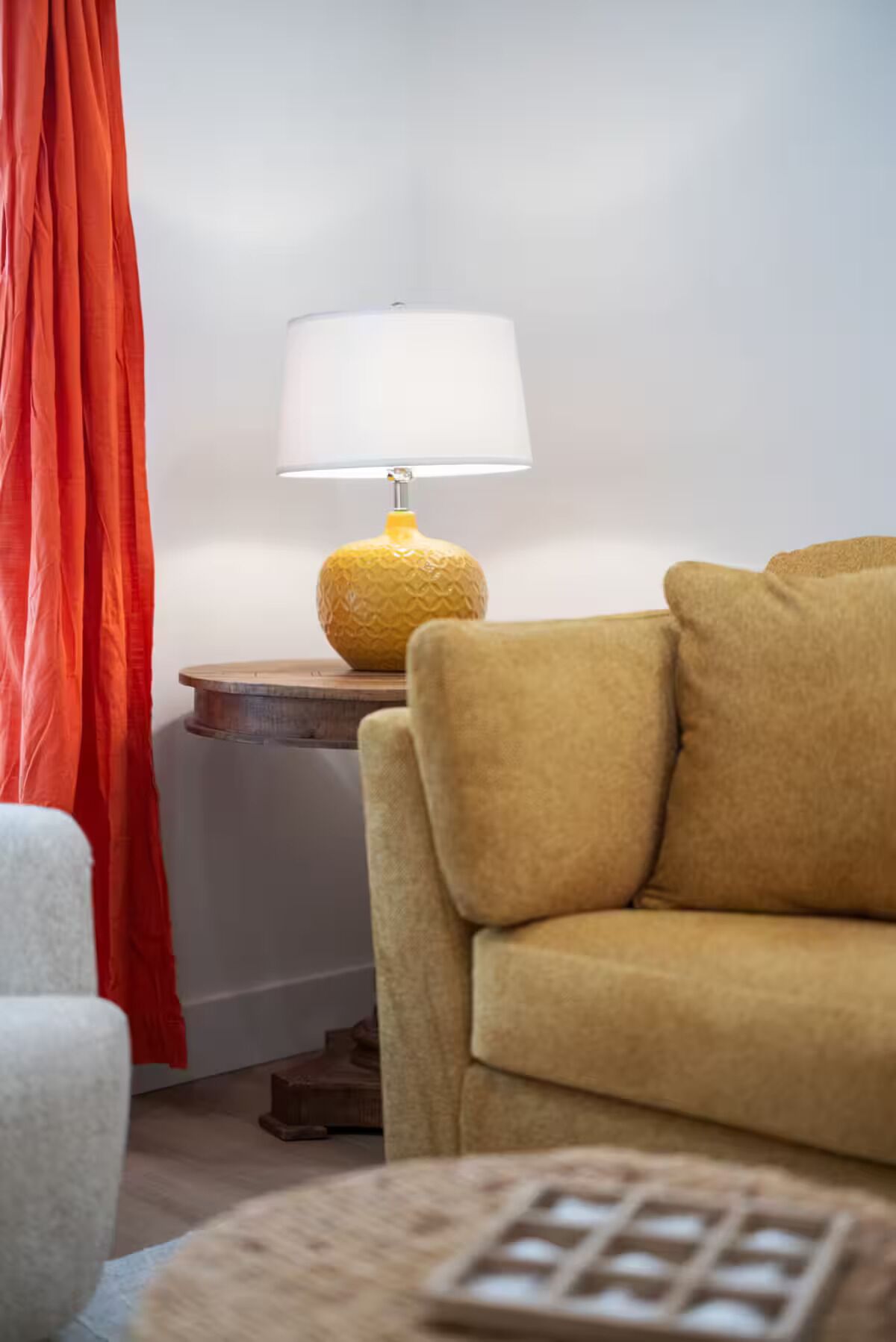 A living room with a yellow lamp on a wooden side table, a yellow sofa, and a white chair.