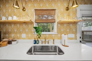 A kitchen with a white countertop, stainless steel sink, and a window with a wooden blind. - Outdoor Movie Theater/ Private POOL & Hot Tub/ Fun (Ocean Isle Beach)