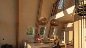 A spacious living area with a high ceiling, a kitchen with modern appliances, and a dining area with bar stools. - Luxury Wellness A-Frame near Zion • Views, Sauna, Cold Plunge & Hot Tub (Glendale)