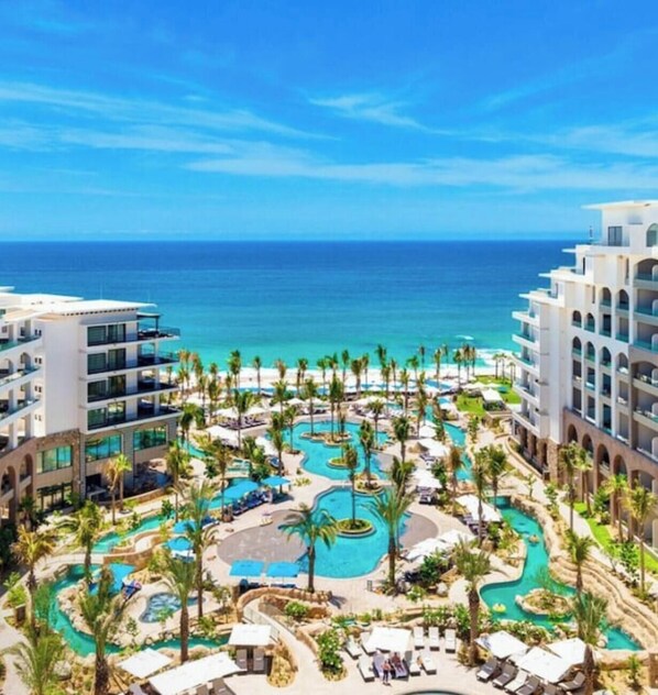 Un resort con varias piscinas, palmeras y vistas a la playa.