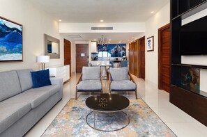 Et moderne hotelværelse med sofa, stole, et spisebord og et køkken i baggrunden.