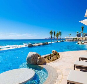 Zona de piscina con vista al océano, sillas de descanso y palmeras.