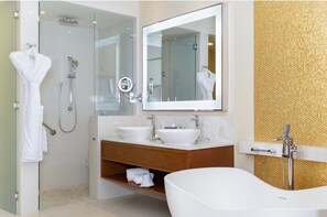 Un baño moderno con ducha envuelta en vidrio, una bañera independiente y un tocador con dos lavamanos.