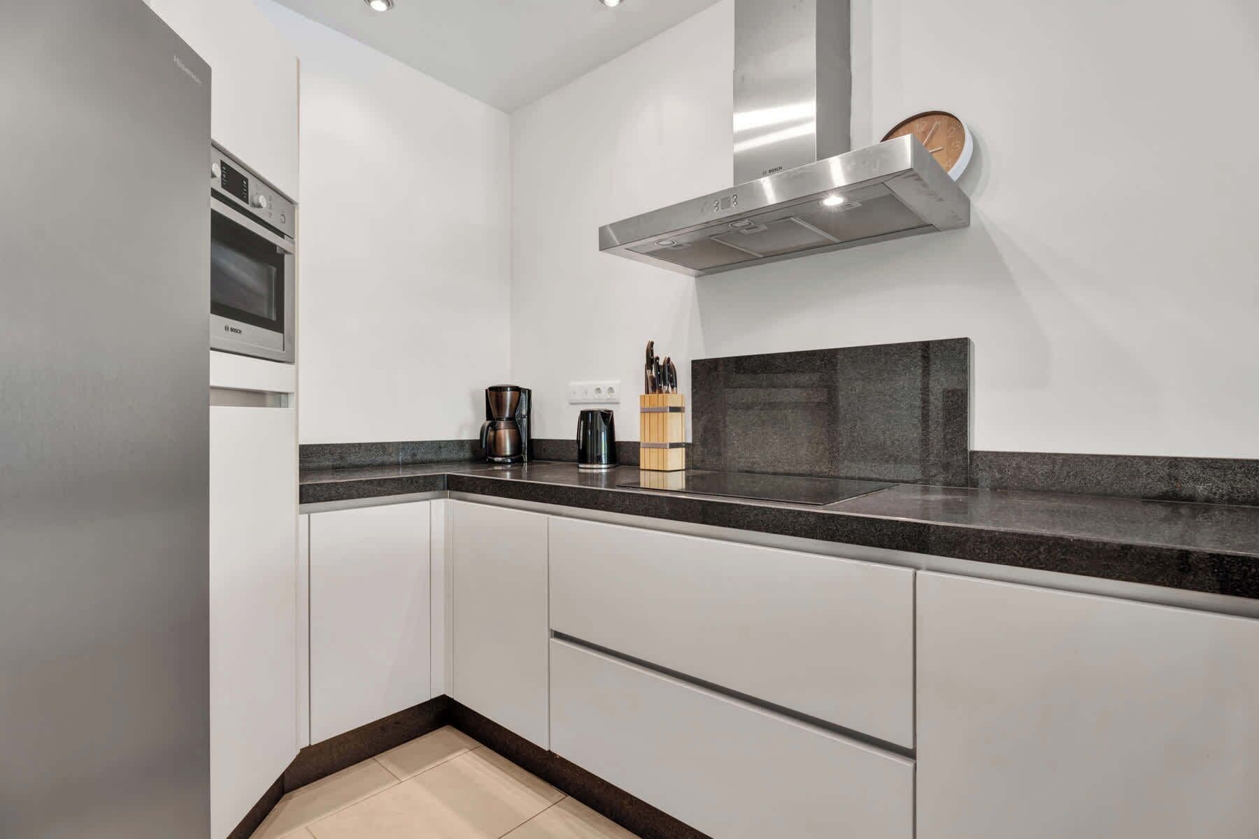 A modern kitchen with white cabinets, a black countertop, and a Bosch range hood.
