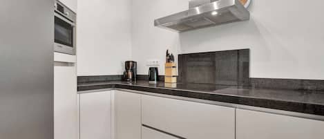 A modern kitchen with white cabinets, a black countertop, and a Bosch range hood.
