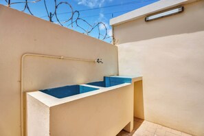 Ein kleines Badezimmer im Freien mit einem blauen Waschbecken und einem Wasserhahn.