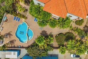 An aerial view of a resort with a swimming pool, lounge chairs, palm trees, and a building with an orange roof. - Bon Bida Buriku with shared pool, Hato (Kralendijk)
