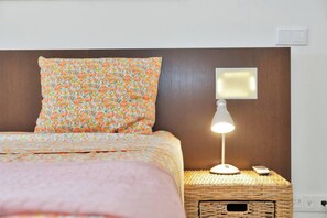 Ein Bett mit einem Blumenkissen und einer Nachttischlampe auf einem gewebten Nachttisch.