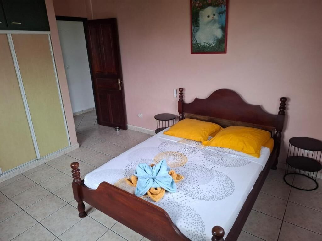 Ein Bett mit Holzrahmen, zwei gelbe Kissen und eine blaue Schleife auf der Bettdecke.