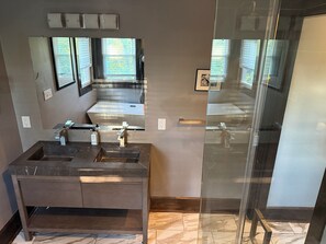 Un baño moderno con un espejo grande, dos lavamanos y una cabina de ducha con mampara de vidrio.