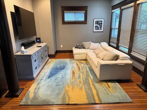 Una sala de estar con un sofá modular, un televisor de pantalla plana, piso de madera y una alfombra estampada.