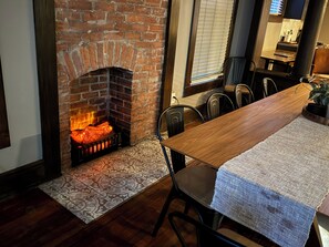 Un comedor con chimenea de ladrillo, pisos de baldosas estampadas y una mesa de madera con sillas.